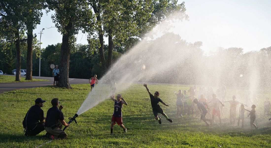 A scenic shot of a water spray in the park and kids playing under it in Lenexa, KS