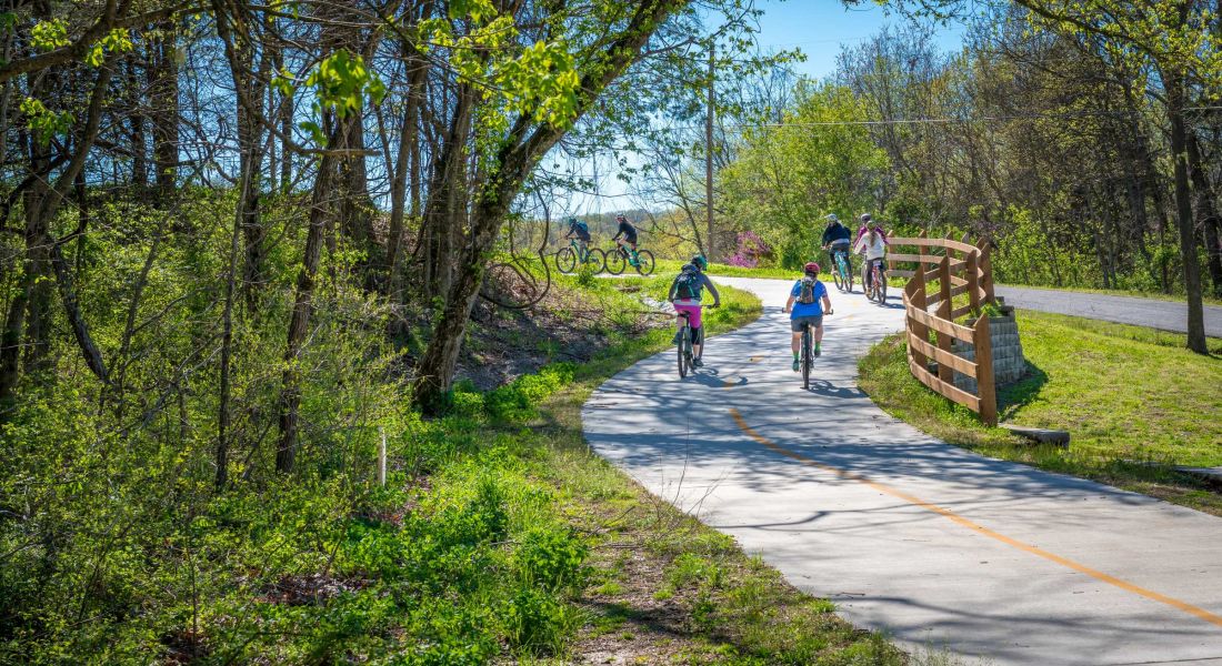Family with kids biking on bike trail with lush park landscape
